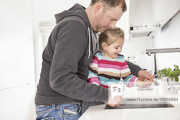Vater und Tochter beim Händewaschen in der Küche