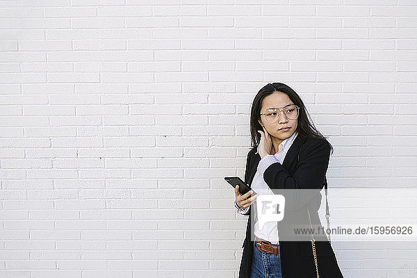 Porträt einer jungen Geschäftsfrau mit Mobiltelefon vor weißer Wand stehend