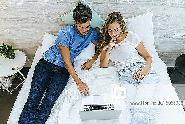 Hochwinkelansicht eines Paares  das einen Film auf einem Laptop anschaut  während es sich zu Hause im Bett entspannt