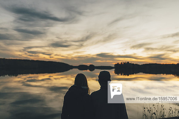 Ehepaar sitzt am See und schaut sich den Sonnenuntergang an