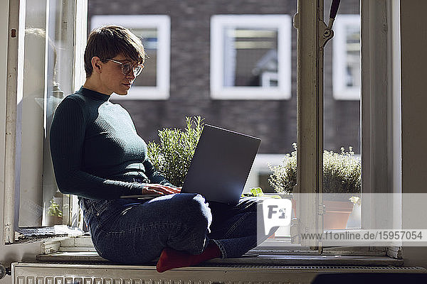Frau sitzt zu Hause mit Laptop am Fenster