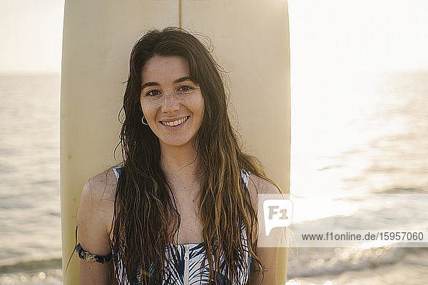 Porträt einer lächelnden jungen Frau mit Surfbrett am Strand  Almeria  Spanien