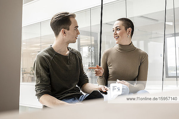 Junge Frau und Mann mit Tablett sprechen am Fenster im Büro