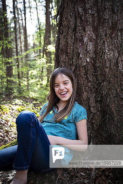 Porträt eines lachenden Mädchens  das sich im Wald an einen Baumstamm lehnt
