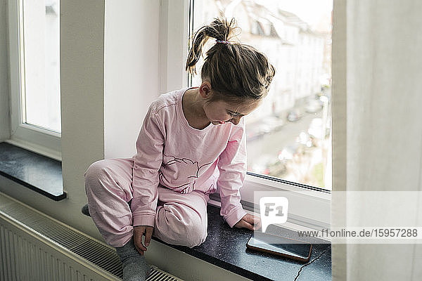 Kleines Mädchen mit Smartphone am Fenster sitzend