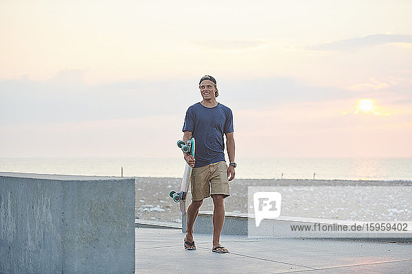 Young man with his skateboard by the beach at sunset.