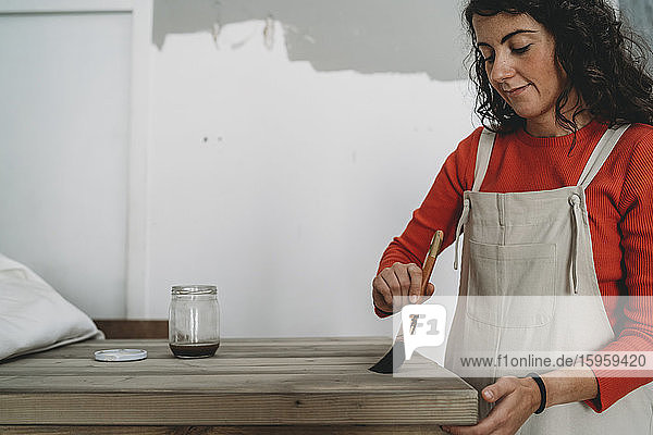 Mittlere erwachsene Frau lackiert Holztisch in ihrem neuen Geschäft