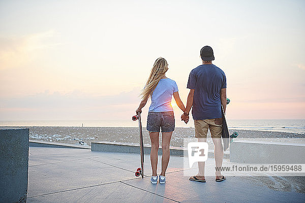 Ein junges Paar  Mann und Frau  skateboarden bei Sonnenuntergang am Strand.