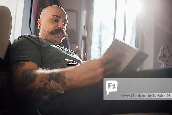 Kahlköpfiger Mann mit Schnurrbart  der während der Corona-Krise ein Buch liest und sich dabei selbst isoliert.