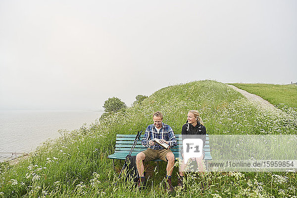 Zwei Wanderer auf einer Bank auf einer Klippe sitzend.
