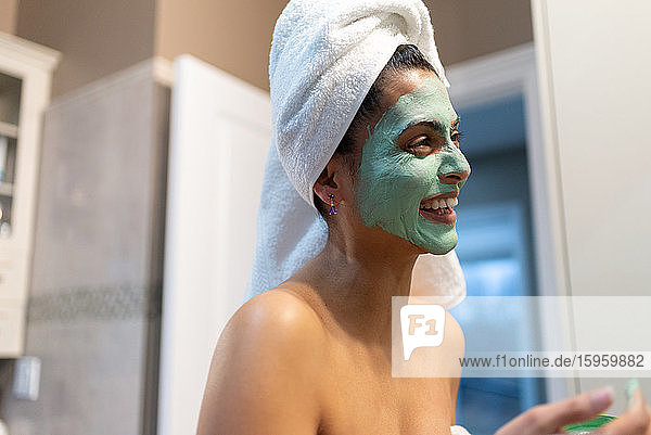 Frau steht im Badezimmer und trägt nach dem Bad eine Gesichtsmaske auf.