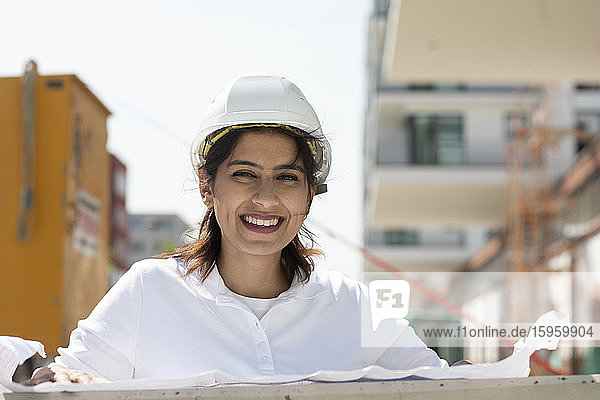 Weibliche Architektin mit weißem Schutzhelm  die auf der Baustelle arbeitet und in die Kamera lächelt.