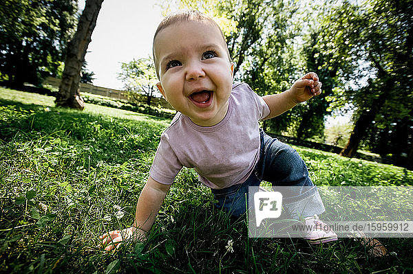 Porträt eines kleinen Mädchens  das auf einem Rasen in einem Park spielt und in die Kamera schaut.