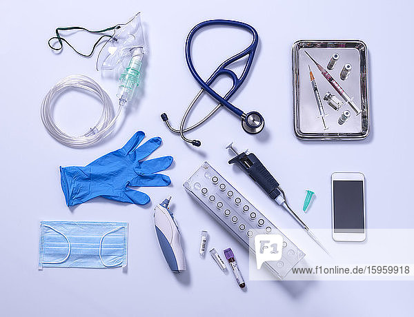 Potentieller Ausweg aus der Abriegelungsphase. Medizinische Ausrüstung auf grauem Hintergrund  Sauerstoffmaske  Stethoskop  Mobiltelefon mit einer Kontaktverfolgungs-App  Impfstoffspritzen  blaue Handschuhe und Digitalthermometer.
