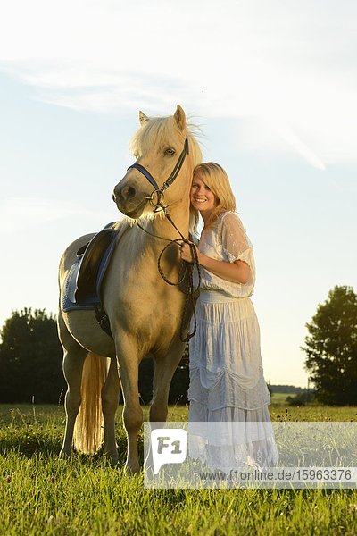 Lächelnde Frau in weißem Kleid mit Pferd auf einer Wiese