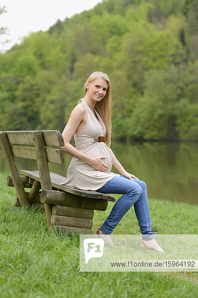 Junge schwangere Frau sitzt auf einer Bank