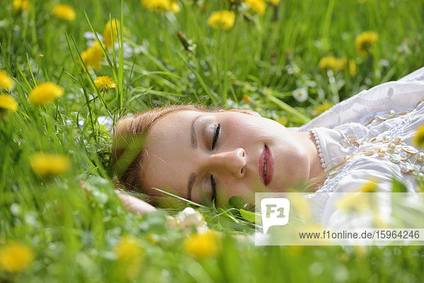 Junge Frau liegt auf einer Löwenzahn-Wiese im Frühling  Portrait