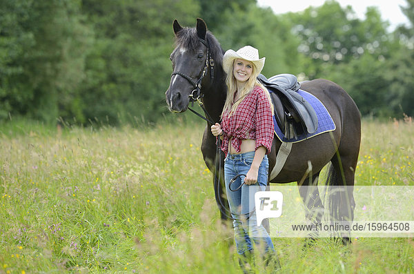 Junge Frau steht neben einem Pferd auf einer Wiese