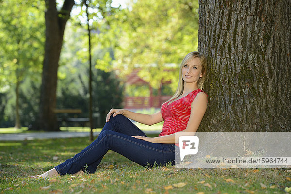 Junge blonde Frau an einem Baumstamm in einem Park