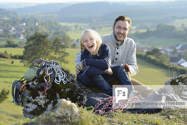 Vater und Sohn sitzen auf einem Felsen mit Kletterausrüstung