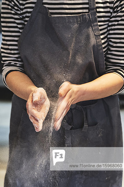 Handwerkliche Bäckerin mit Schürze  die ihre Hände mit Mehl betupft.