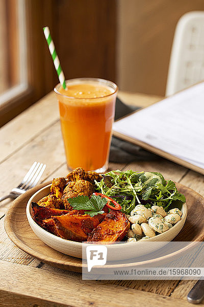 Nahaufnahme eines Glases mit Karottensaft und einer Schüssel mit gemischtem Gemüse in einem Cafe.