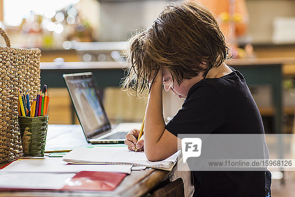 6-jähriger Junge  der eine Fernschulung mit seinem Lehrer hat und sich dabei auf das Schreiben konzentriert.