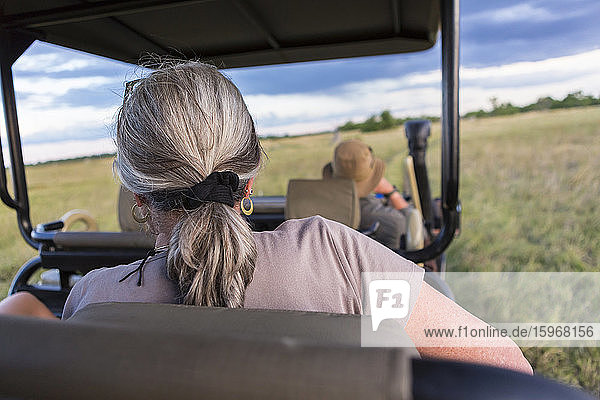 Eine Frau mit grauen Haaren sitzt in einem Safari-Fahrzeug und beobachtet Wildtiere