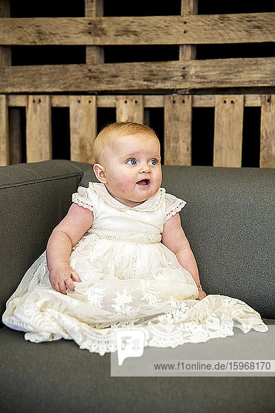 Porträt eines kleinen Mädchens in weißem Gewand während der Taufzeremonie in einer historischen Scheune.