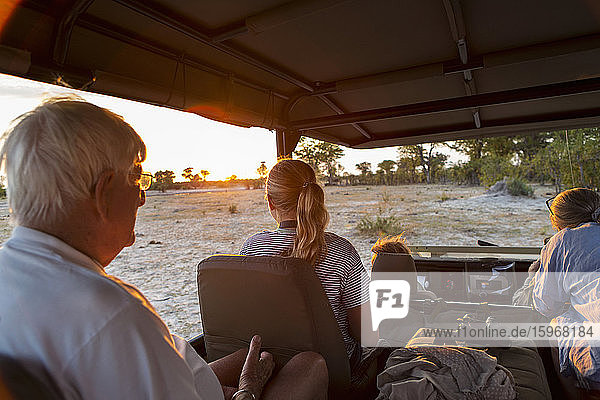 Drei Generationen einer Familie auf Safari  in einem Jeep bei Sonnenuntergang.