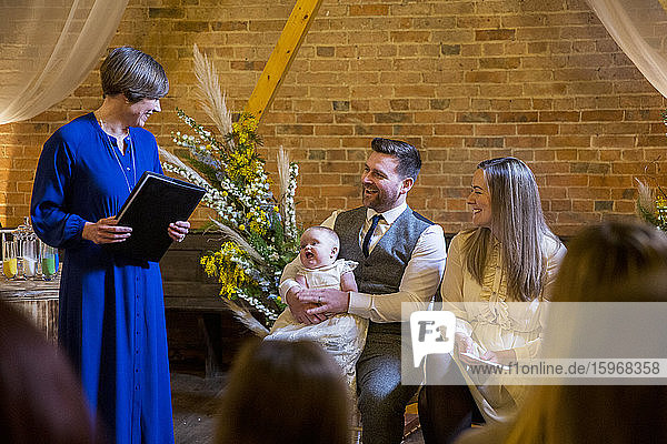 Zelebrant bei der Taufzeremonie für Eltern und ihre kleine Tochter in einer historischen Scheune.