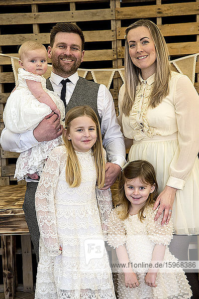 Portrait of smiling parents with their three young daughters during naming ceremony in an historic barn.