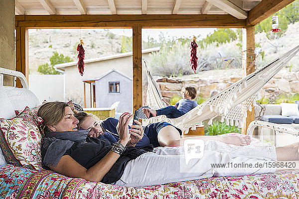 Mutter und Tochter liegen zusammen auf einem Bett im Freien und schauen auf den Bildschirm eines Smartphones