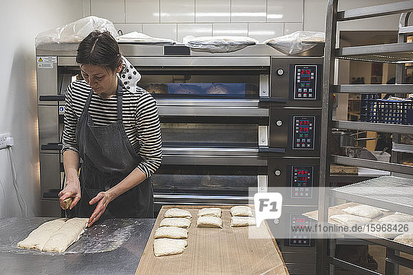 Handwerkliche Bäckerei  die spezielles Sauerteigbrot herstellt  ein Bäcker  der Teig für Brötchen schneidet.