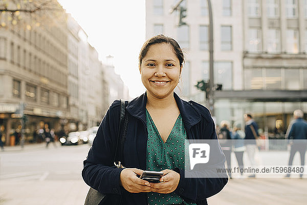 Porträt einer lächelnden Unternehmerin mit stehendem Telefon in der Stadt