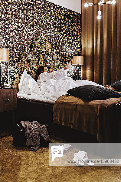 Mittlere erwachsene Frau  die mit ihrem Freund im Hotelzimmer im Bett liegt