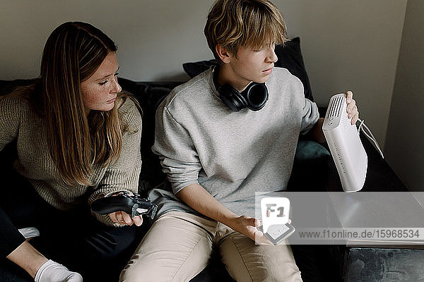 Teenage boy checking Wi-Fi router while sitting with friend on sofa at home