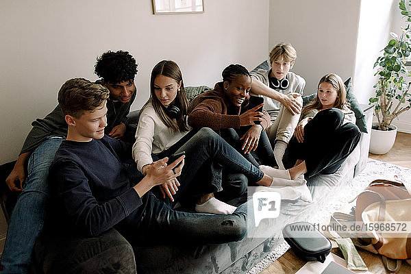 Männliche und weibliche Freunde im Teenageralter benutzen Mobiltelefone  während sie zu Hause auf dem Sofa sitzen