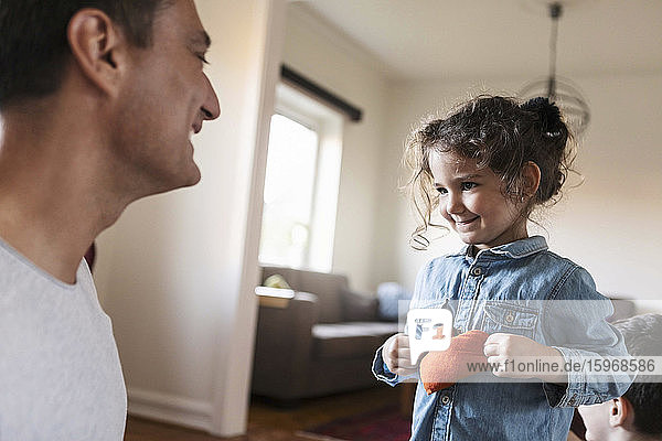 Smiling daughter showing stuffed heart shape to father at home