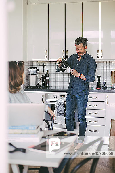 Man pouring coffee having fun conversation with woman at home