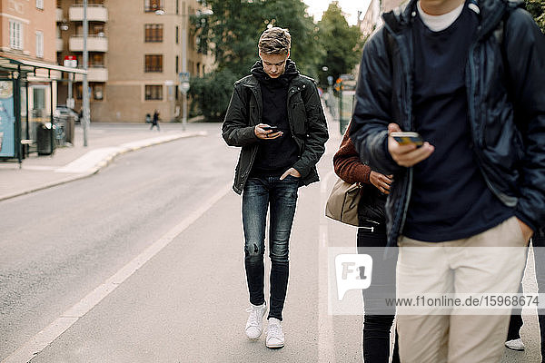 Teenage boy using smart phone while walking on street in city