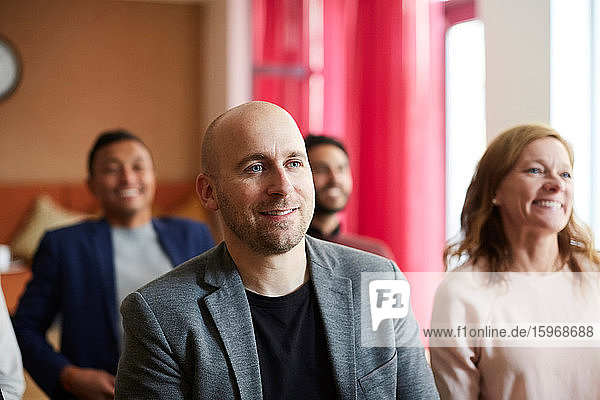 Lächelnder männlicher Unternehmer sitzt mit Kollegen in Bürobesprechung am Arbeitsplatz