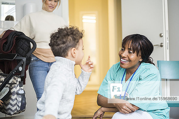 Boy talking to smiling female nurse while mother standing in background at medical clinic