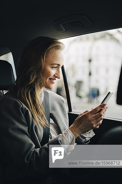 Lächelnder Unternehmer benutzt Smartphone  während er im Taxi sitzt