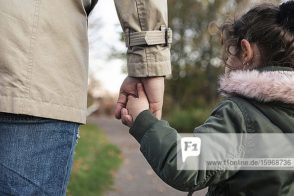 Daughter holding hands with father in park during autumn