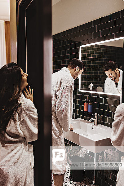 Lächelnde Frau sieht Mann an  der im Badezimmer vor dem Spiegel steht