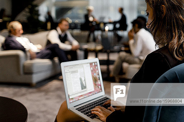 Businesswoman using laptop with colleagues sitting in background at office