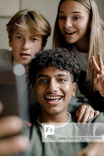 Lächelnder Teenager  der sich mit Freunden über sein Mobiltelefon zu Hause selbstständig macht