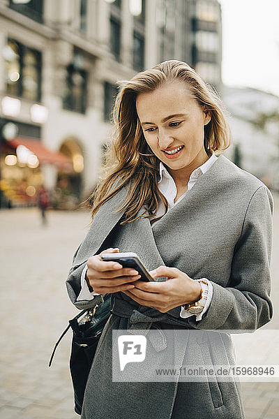 Smiling entrepreneur using smart phone while standing in city