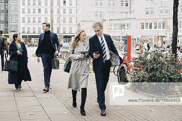 Geschäftsmann zeigt einer Kollegin ein Smartphone beim Spaziergang in der Stadt